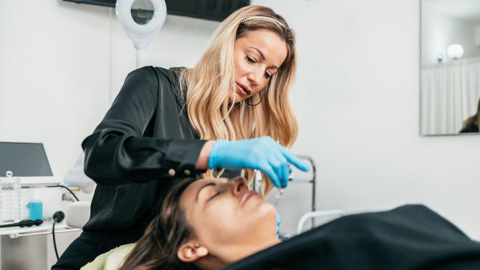 A woman administering lip filler to another woman laid on a medical bed