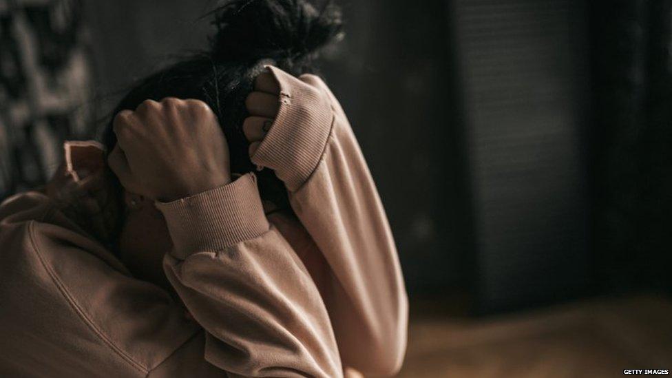 Woman covering face on a bed looking upset