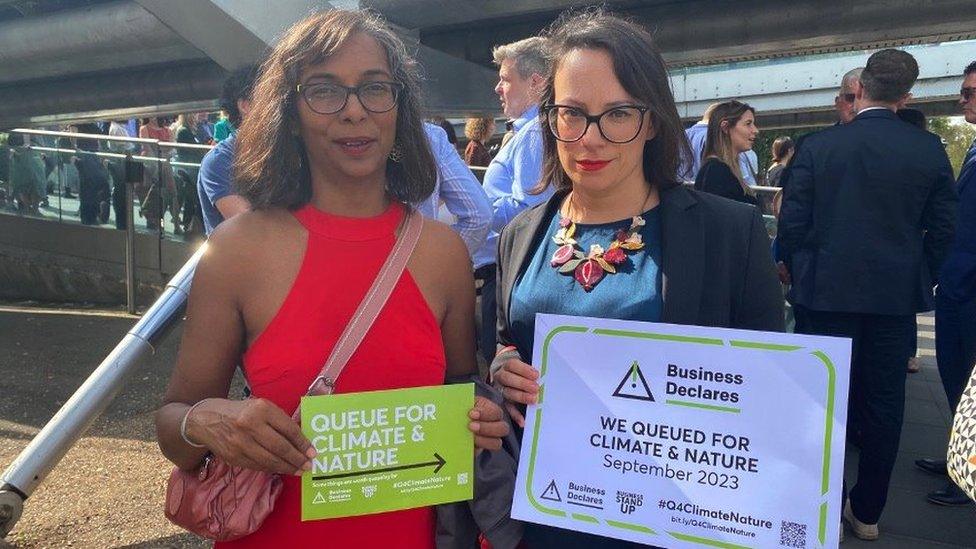 Two woman stand side by side at demonstration, holding climate action signs