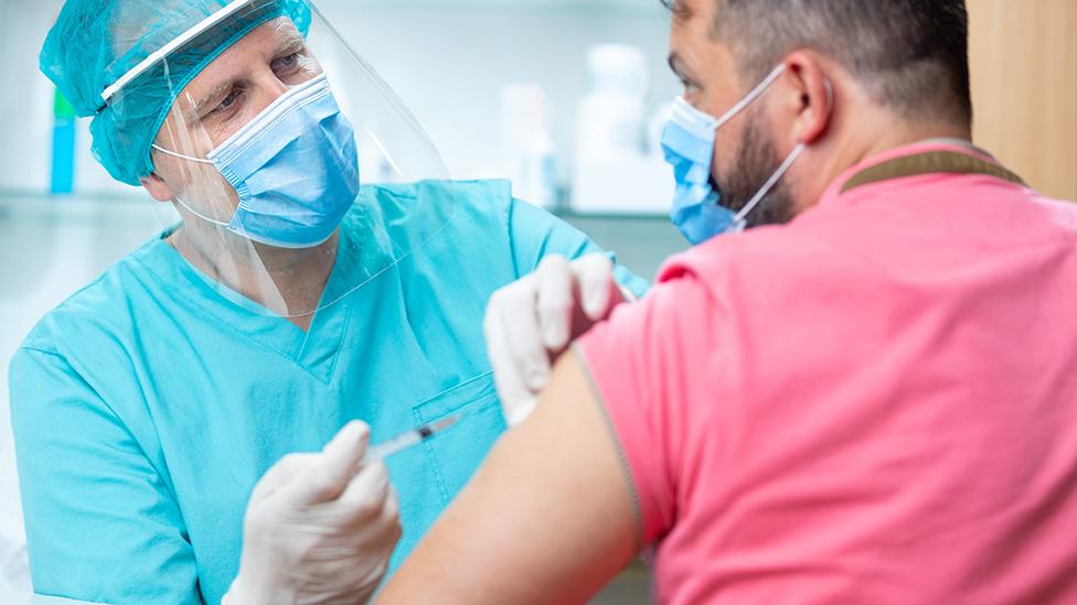 Medic administers jab to man in pink shirt