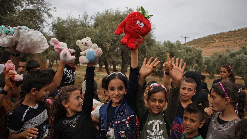 Syrian children raise up toys that were given to them by a Syrian man living in Finland and calling himself "The Toy Smuggler"