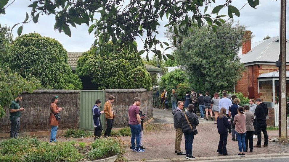 A line of people waiting to inspect a house