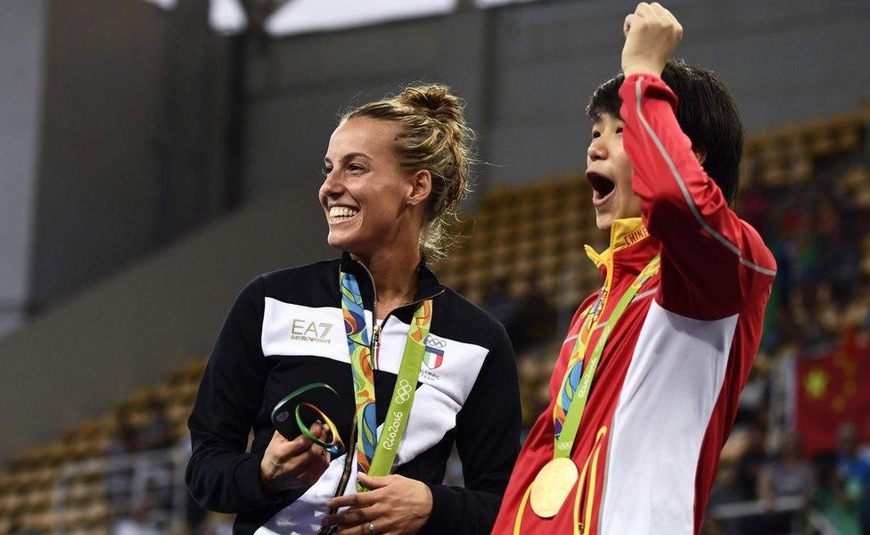 Gold medallist China"s Shi Tingmao (R) and bronze medallist Italy"s Tania Cagnotto react as Silver medallist China"s He Zi (unseen) receives a marriage proposal from Chinese diver Qin Kai during the podium ceremony