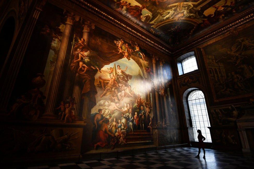 A gallery assistant poses beside a fresco during the reopening of The Painted Hall, Old Royal Navy College in London, Britain, 20 March 2019.