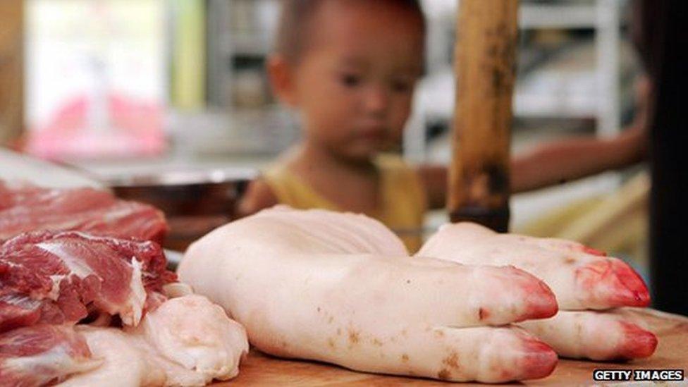 A child stands next to pig trotters at a market on the outskirts of Chengdu