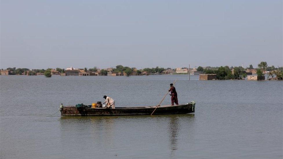 A man rows a boat with submerged houses in the background, following rains and floods during the monsoon season in Mehar, Pakistan August 31, 2022.