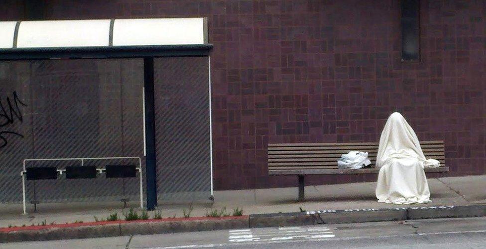 A person covered in white material waits at a bus stop