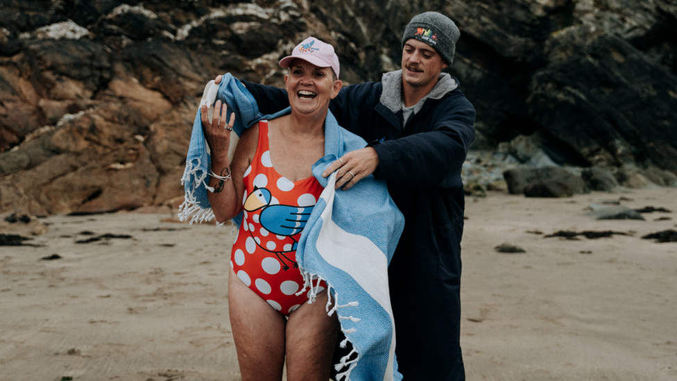 A man wrapping a towel around an older woman in a swimsuit on a beach