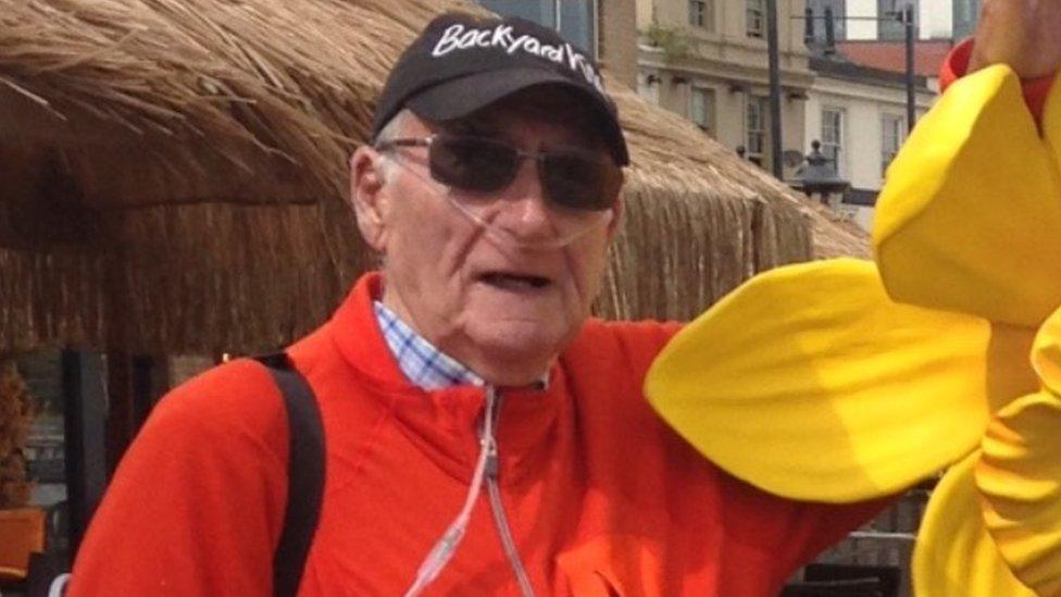 John wearing a portable oxygen tank while standing next to a yellow daffodil