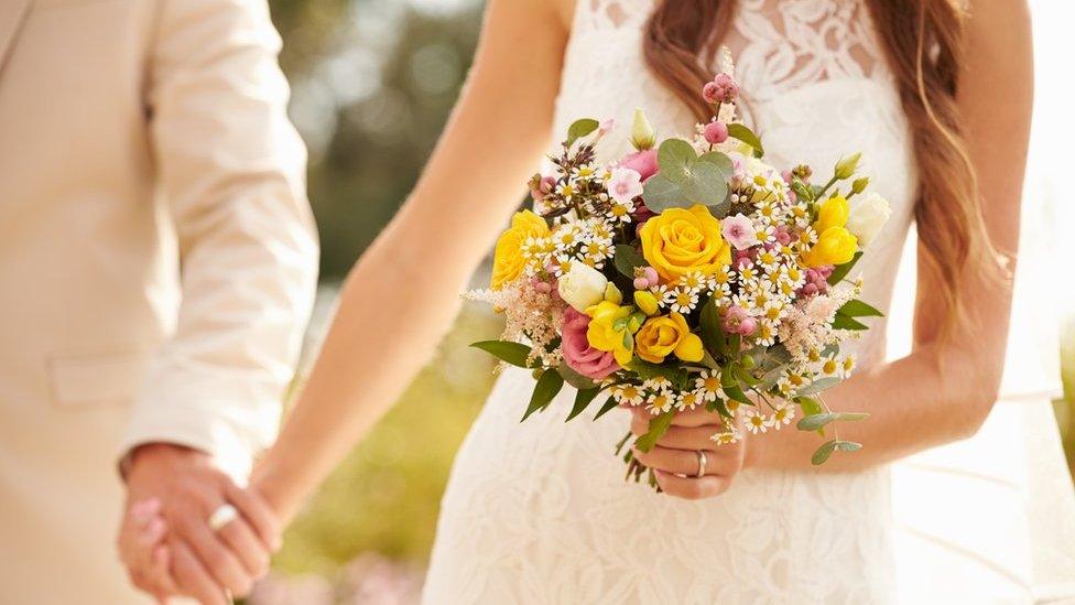 A stock picture of an unidentified straight couple holding hands at their wedding