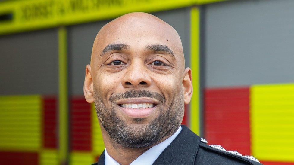 Sam Allison smiles at the camera in front of a blurred fire engine