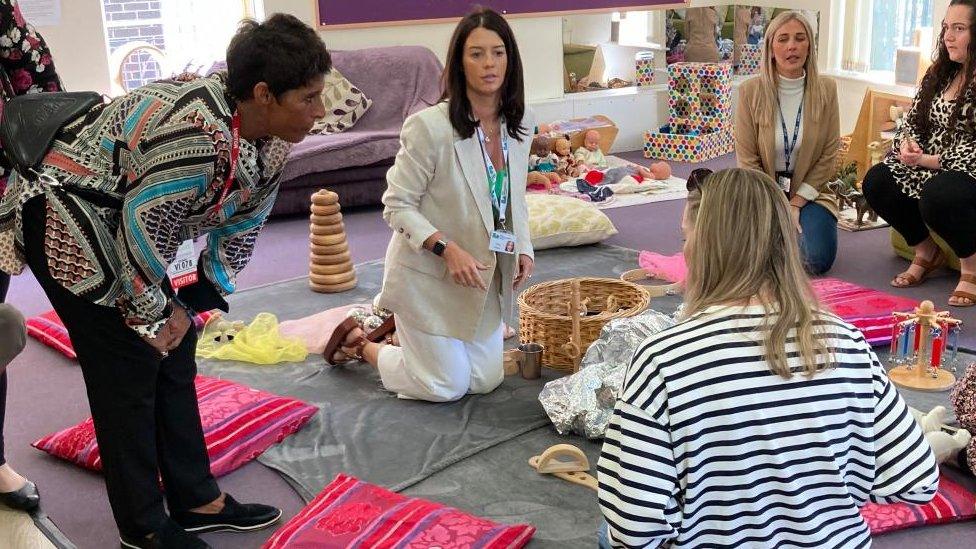 Fatima Whitbread bends down to talk to mothers kneeling on a play mat