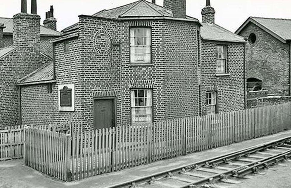 Old picture of the building with plaque and railway line