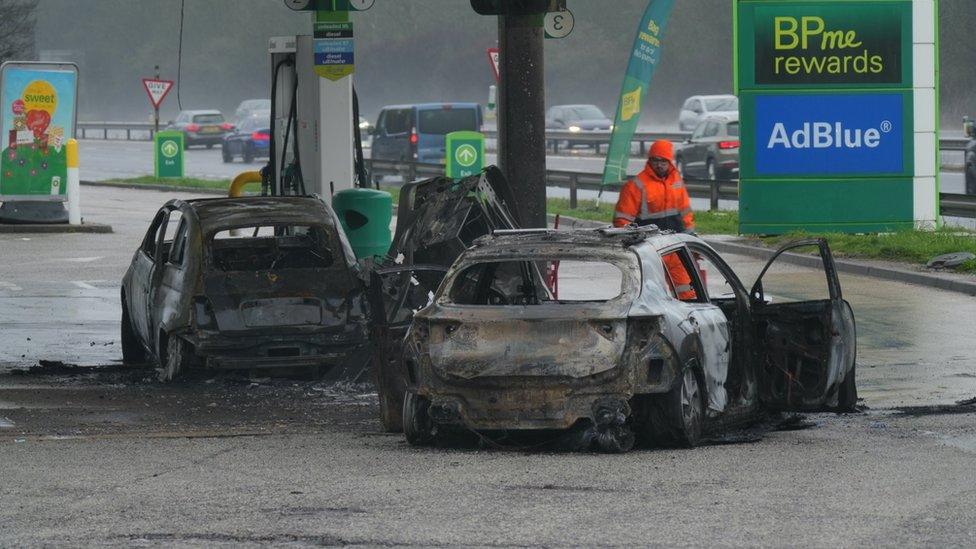 The burnt out shells of two cars on a petrol forecourt.