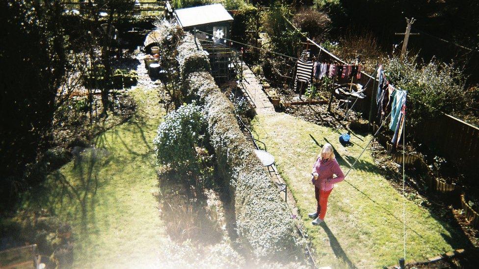 Photo taken from upstairs window showing woman standing alone in a back garden