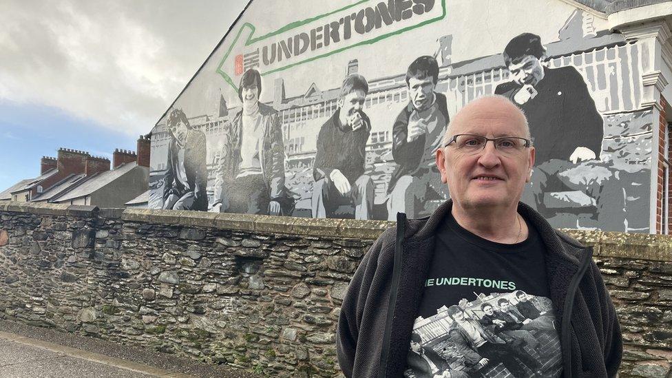 Greg McCartney standing in front of Undertones mural