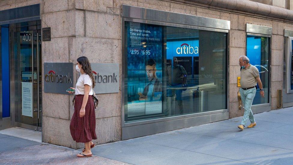 People in masks walk past a Citi ATM