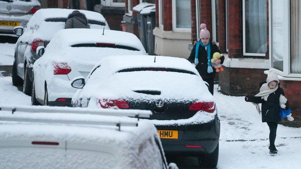 Child running in the snow, near road with snowy cars parked