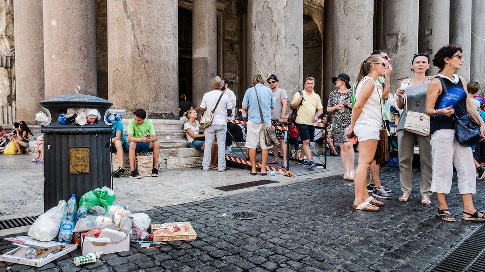 Tourists stand next to a bin overflowing with waste in front of the Ancient Pantheon, in central Rome on July 27, 2015