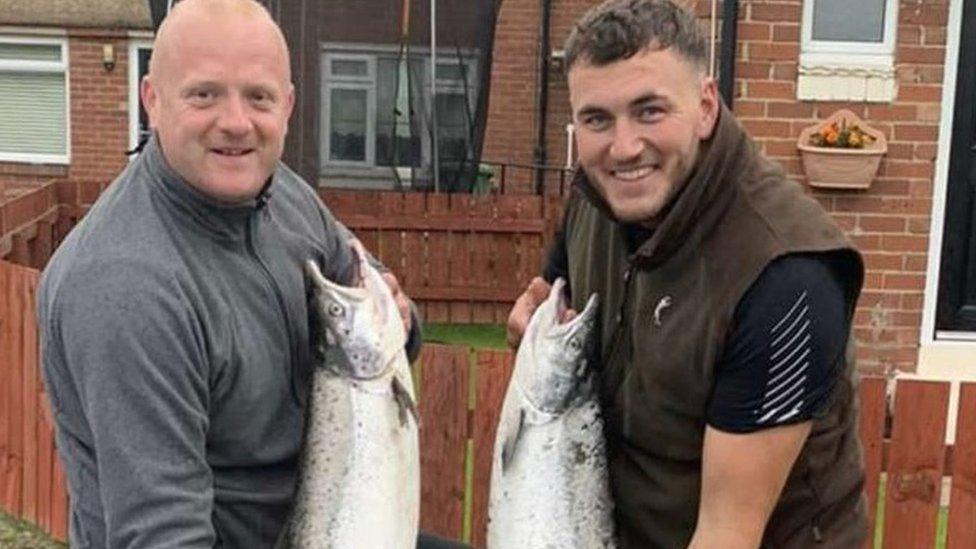 Two men each holding a large fish up to camera