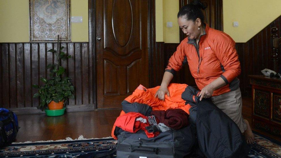 Lhakpa Sherpa packing her bags with climbing equipment, standing inside a hallway