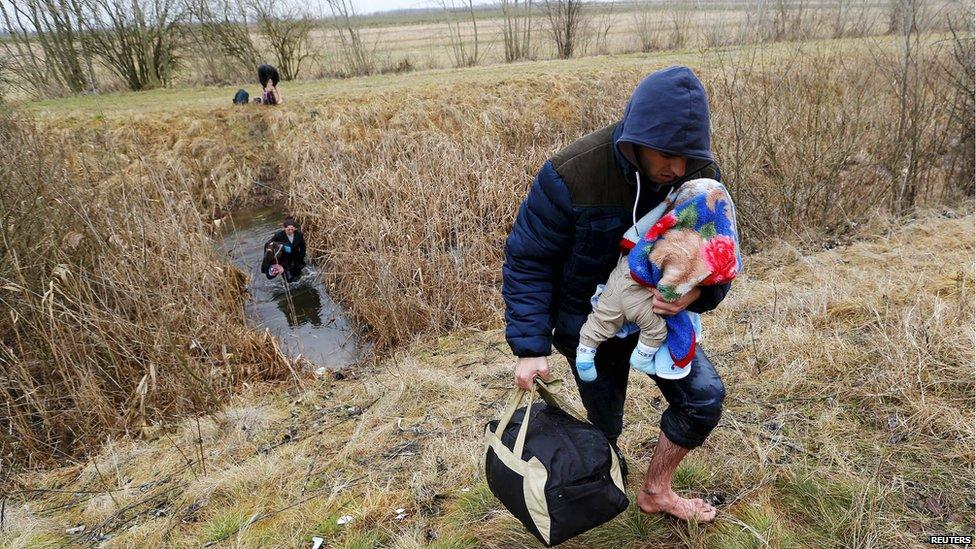 A Kosovar man wades through water while carrying his child as they illegally cross the Hungarian-Serbian border near the village of Asotthalom, Hungary, in this February 6, 2015 file photo