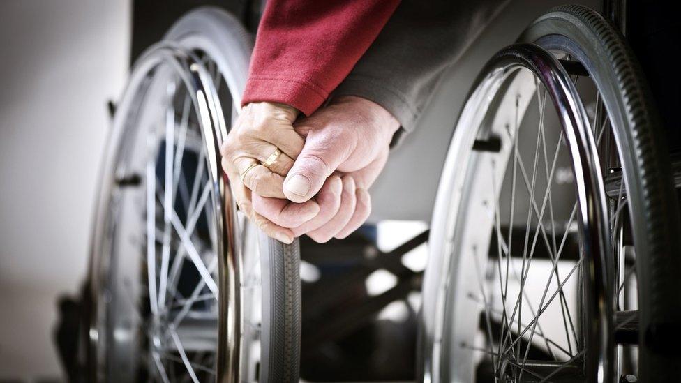 Elderly couple hold hands with wheelchair