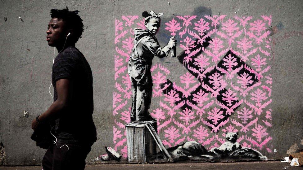 A man walks past a recent artwork by street artist Banksy in Paris