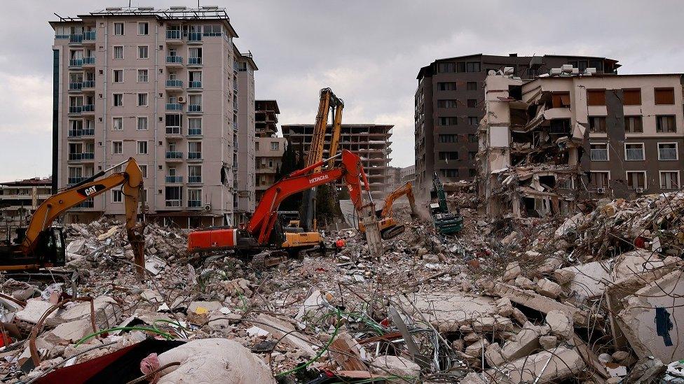 Workers clean the rubble of a collapsed building in the aftermath of a deadly earthquake