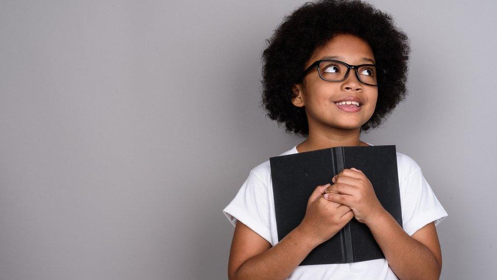 A boy holds notebook and looks thoughtful