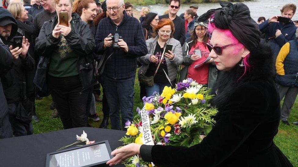 Woman dressed in black with wreath and coffin