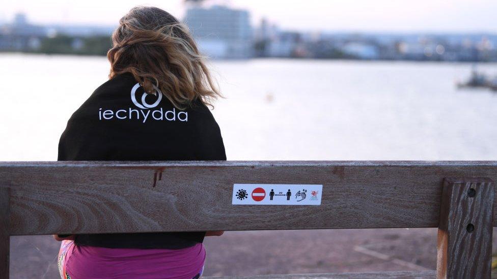 Woman sat at park bench in Cardiff with warning sign on back