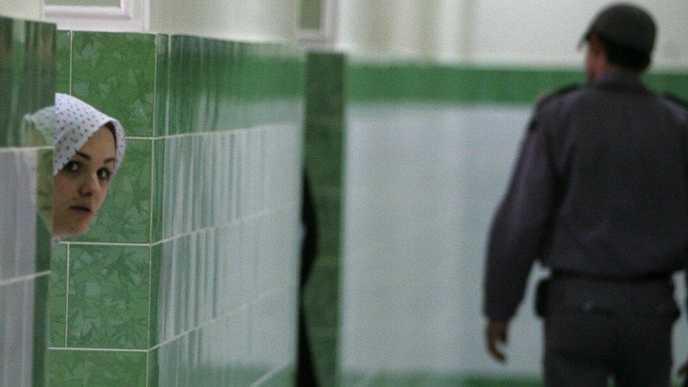 An Iranian inmate peers from behind a wall as a guard walks by at the female section of the infamous Evin jail