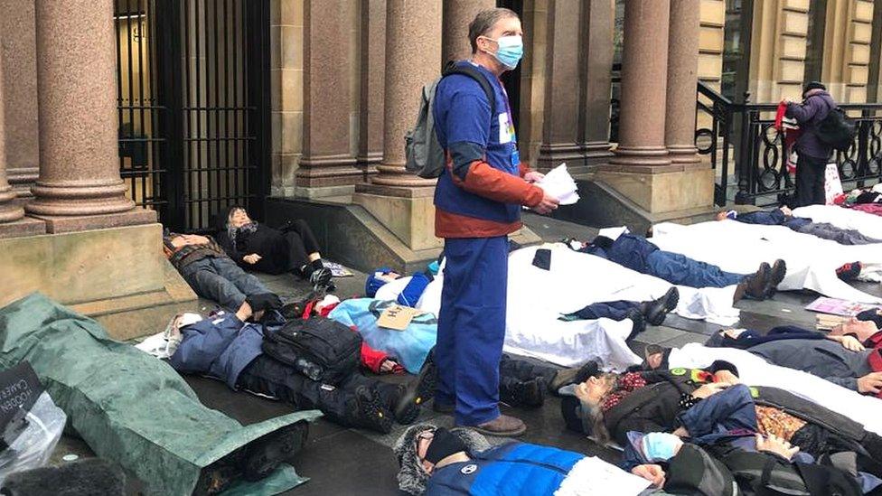 Protestors are lying down in front of the offices of an assets management company