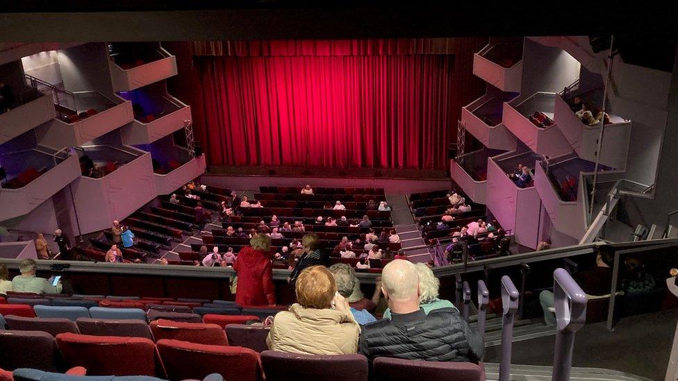 Modern theatre auditorium from the back of the upper circle, with red curtains drawn across the stage