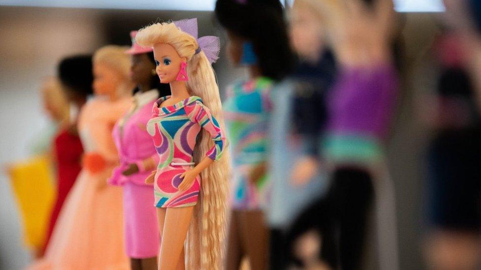 The 1992 Totally Hair Barbie, wearing a green, pink and purple swirl design dress and long hair, alongside other Barbies