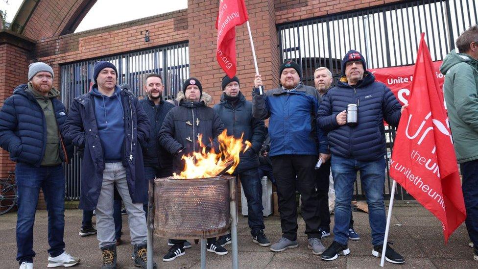 men keeping warm around a fire while flying Unite the Union flags