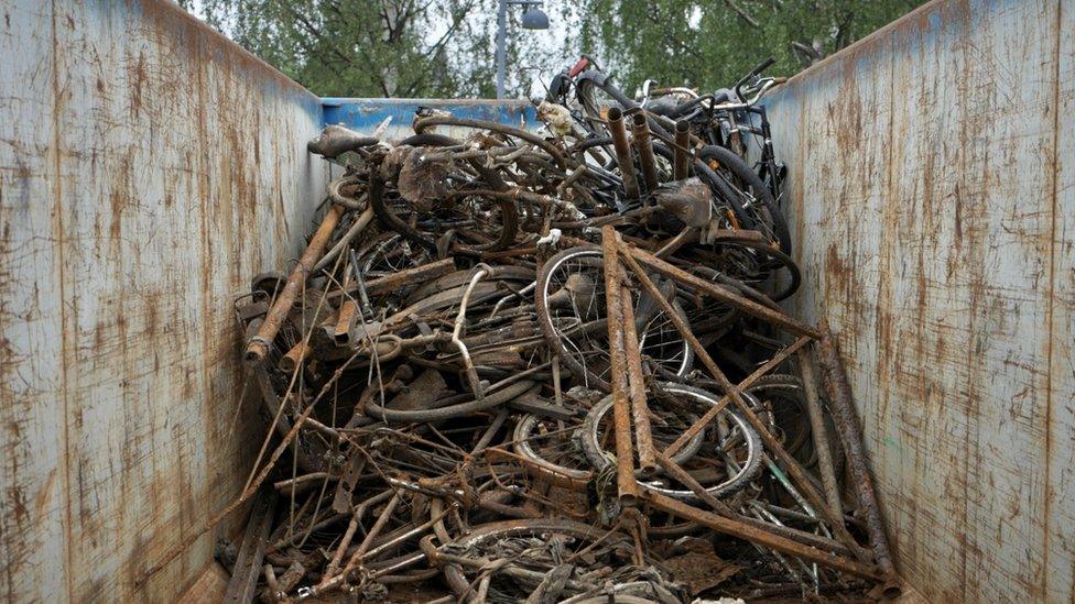 Discarded old rusty bikes lie in a large skip