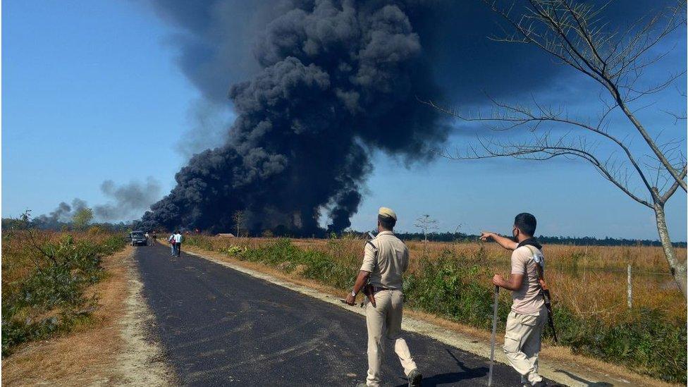 Policemen gesture as they ask people to move to a safer place as smoke rises following an explosion at an oil well