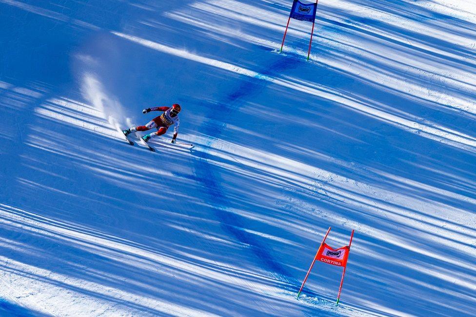 A woman dressed in red skiiing gear skis down a steep, snow-covered slope.