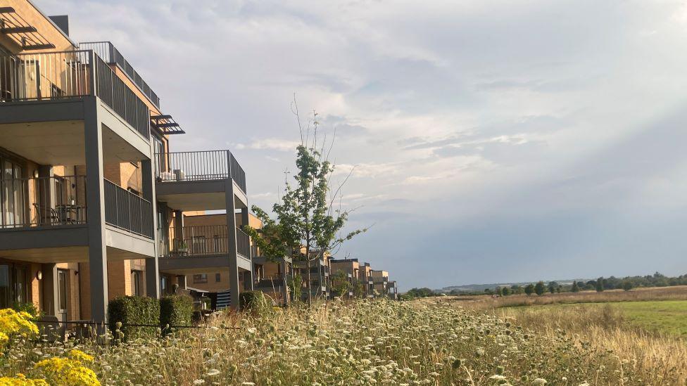 A row of modern apartment blocks overlooking green fields and meadows.