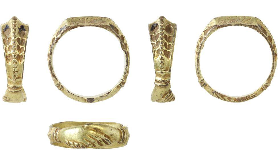 Five views of a late medieval gold ring. Two of the views show the band on its side. It has a flat top in the style of a signet ring. Its band is decorated with both its shoulder views showing decorations. The base has been decorated with clasped hands