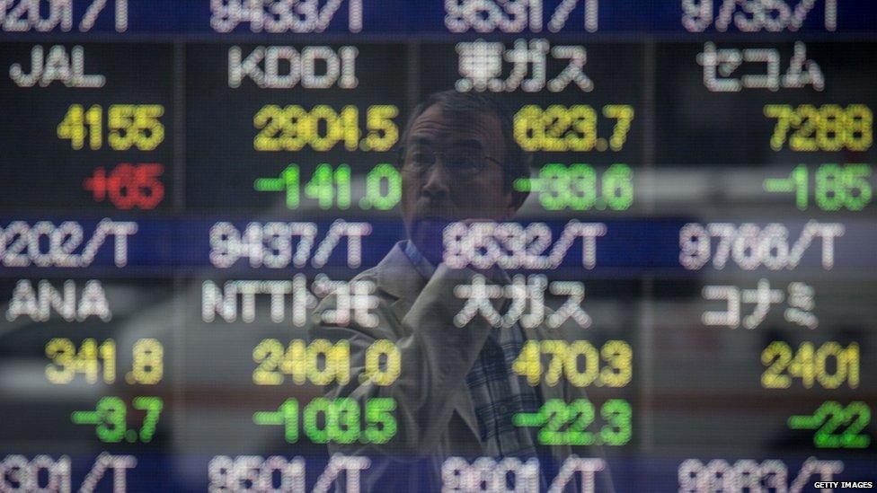 A man looks at a screen showing global stock market information on the street in Tokyo