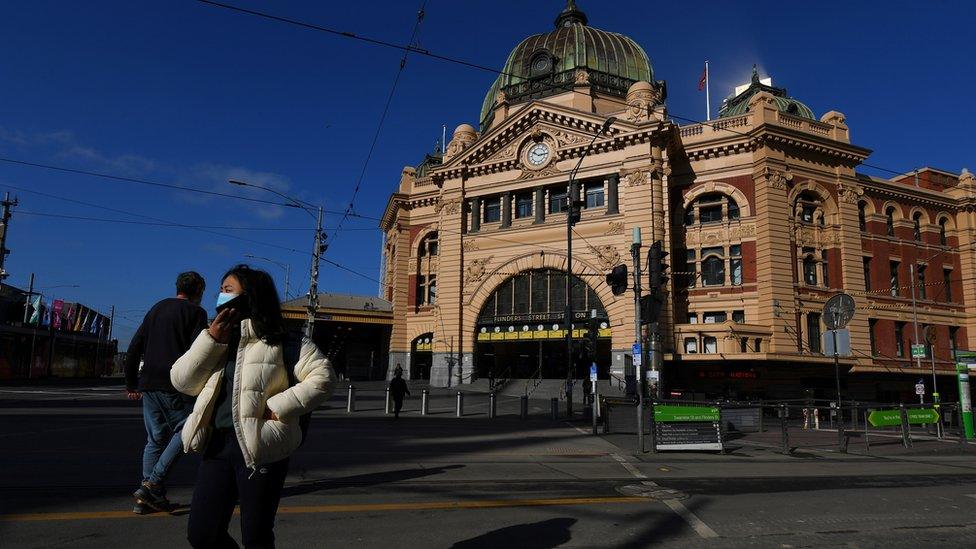 Person wearing a mask walks past a deserted Flinders Street Station