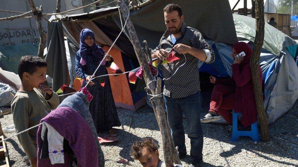 A man hangs flags outside his family tent at a makeshift camp for migrants and refugees at the Greek-Macedonian border