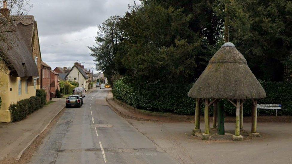 Rural road with small thatched domed structure in foreground and houses to the left