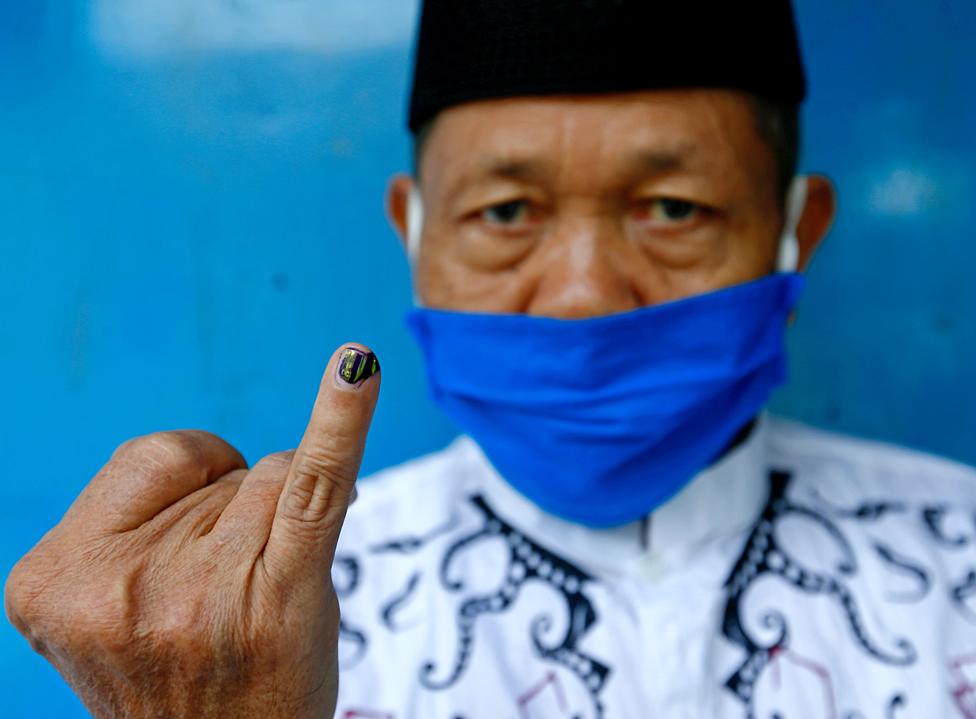 A man wearing a face mask holds up his ink-stained finger