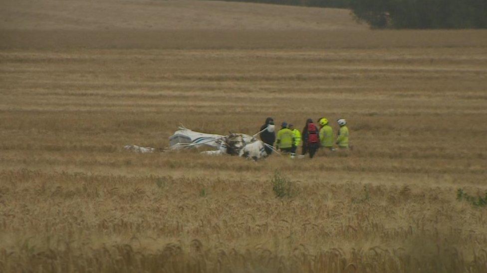 The crash plane in the field with emergency personnel around it