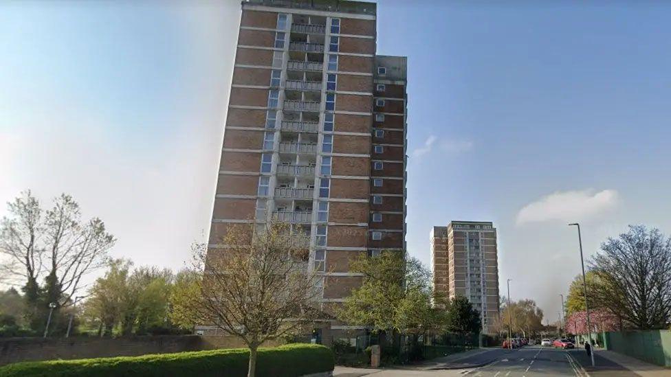 Two high towers in Kirkby with trees and a green bush