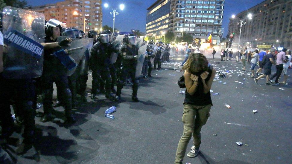 A woman ducks away from riot police in Romania